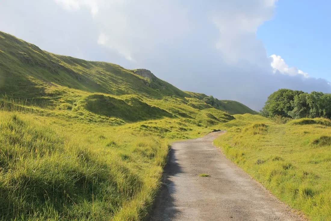 The Cotswold Way winding across open grassland and limestone hummocks on Cleeve Hill under a partly cloudy sky