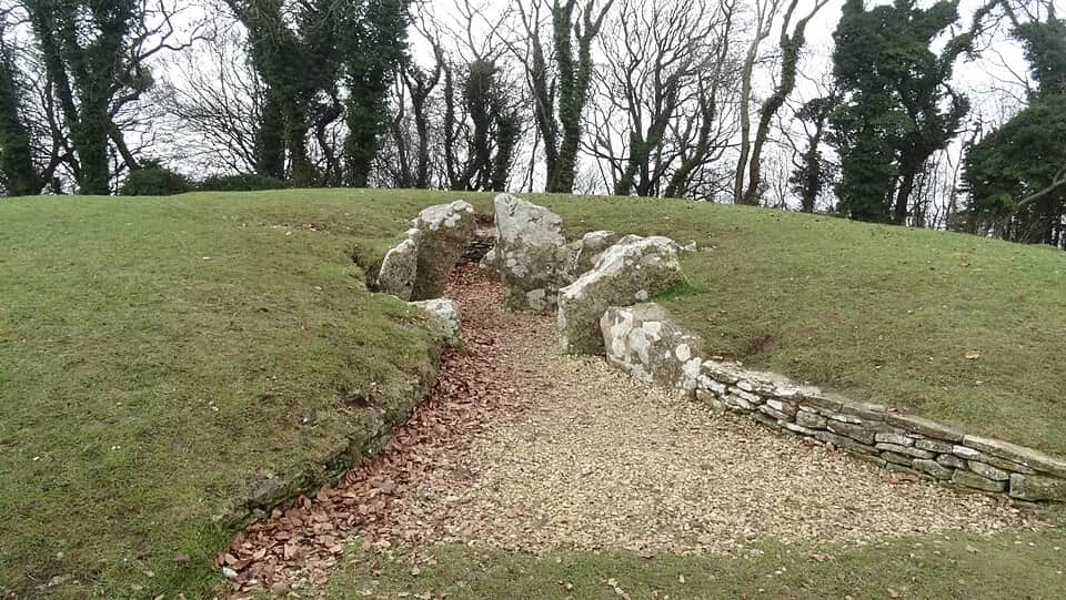 Stone entrance and chambers of Nympsfield Long Barrow set into a grassy mound with bare winter trees beyond