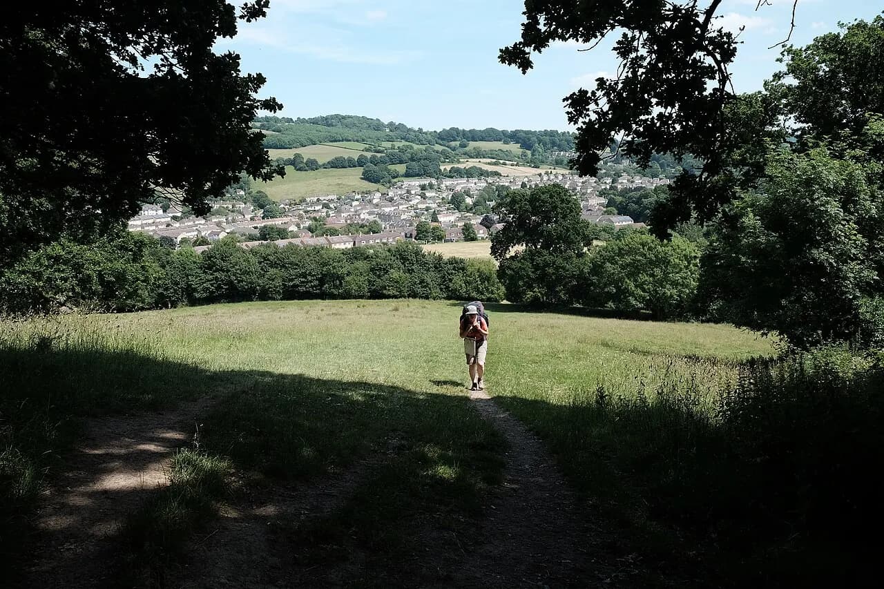 Hiker with a backpack walking the Cotswold Way through a grassy field