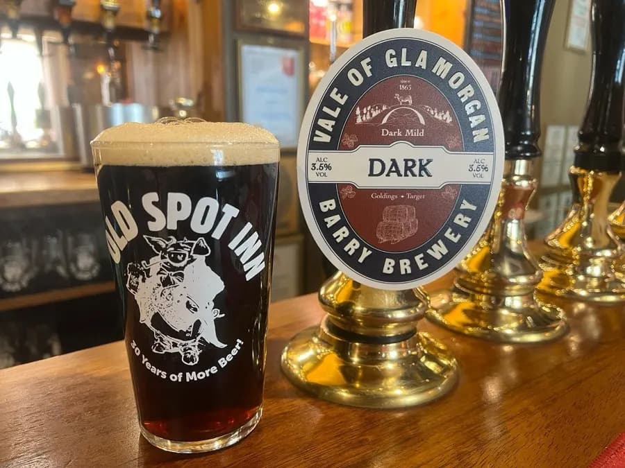 Pint of dark mild beside a brass handpull at The Old Spot Inn