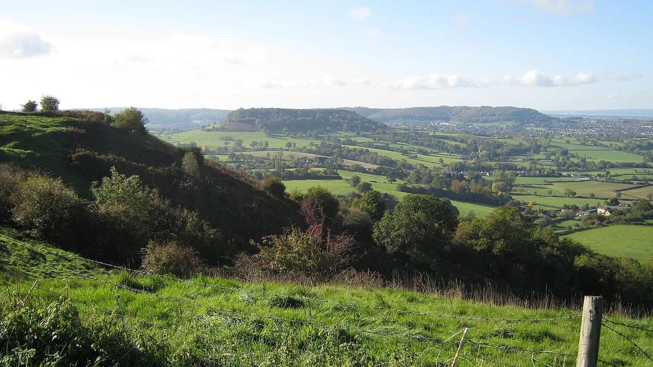 Panoramic view from Coaley Peak across rolling green fields and hedgerows toward a town in the valley