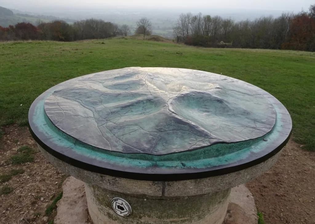 Bronze relief toposcope on a Cotswold stone plinth at Haresfield Beacon, with a Cotswold Way acorn marker and views over the Severn Vale