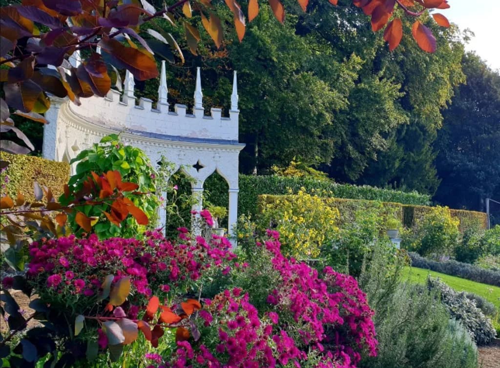 Gothic folly and summer planting in Painswick Rococo Garden, with pink flowers and woodland beyond