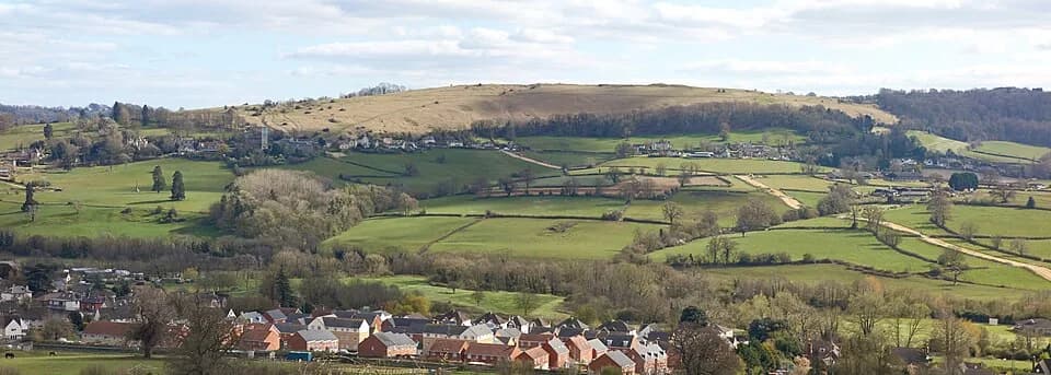 Panoramic view of the flat-topped grassy plateau of Selsley Common rising above green fields and housing in the Stroud valleys