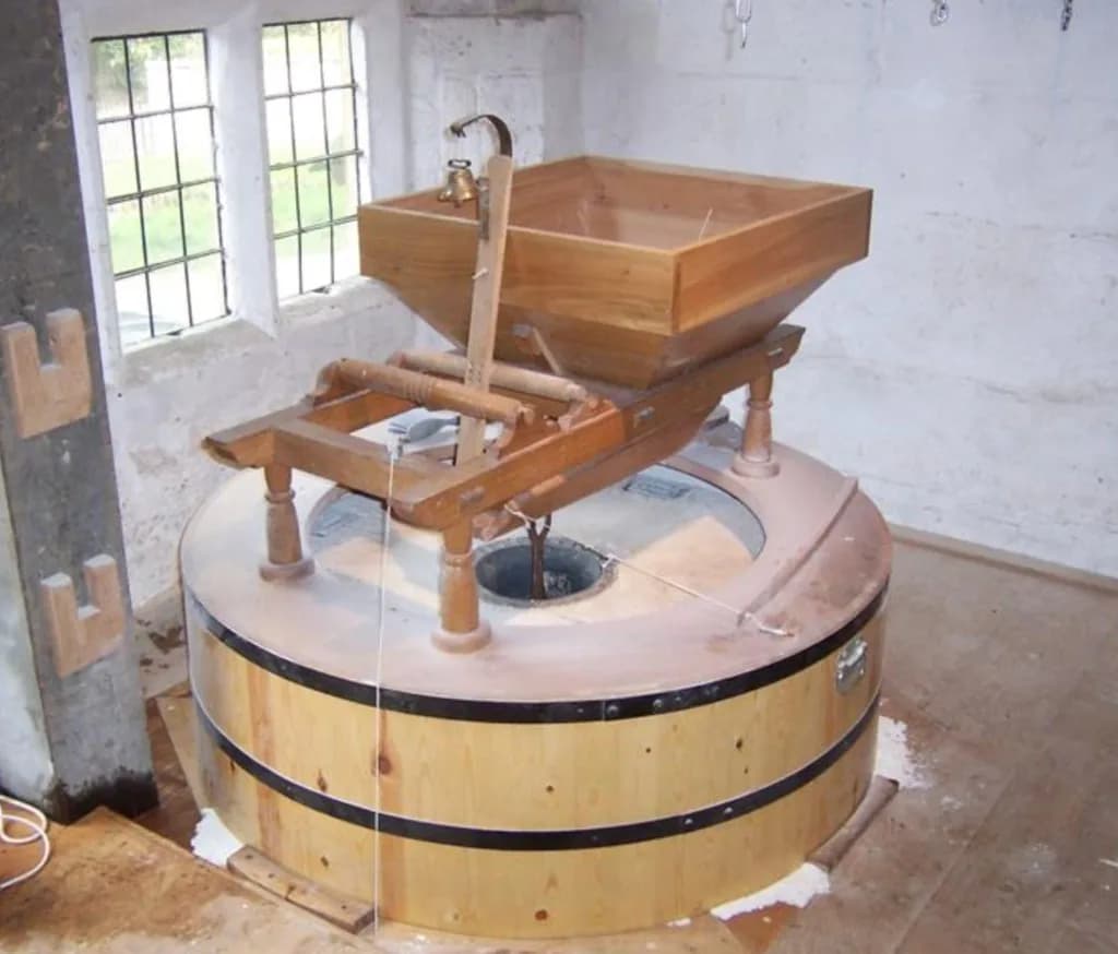 The restored millstones and wooden grain hopper inside Stanway Watermill, Gloucestershire