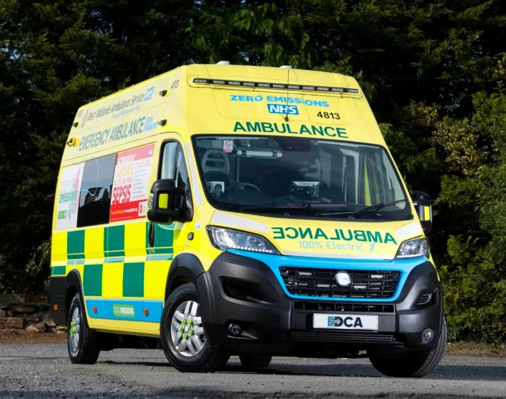 Yellow NHS emergency ambulance parked beside woodland
