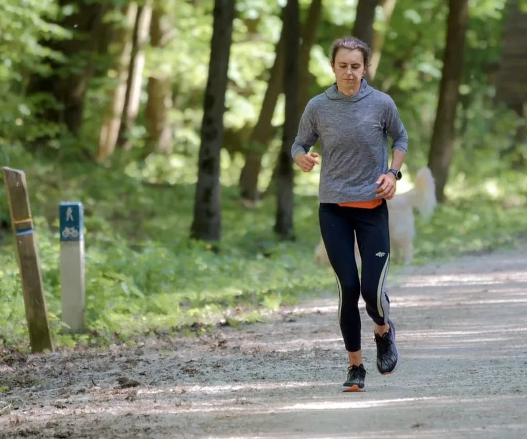 Runner on a sunlit forest trail with a dog following behind
