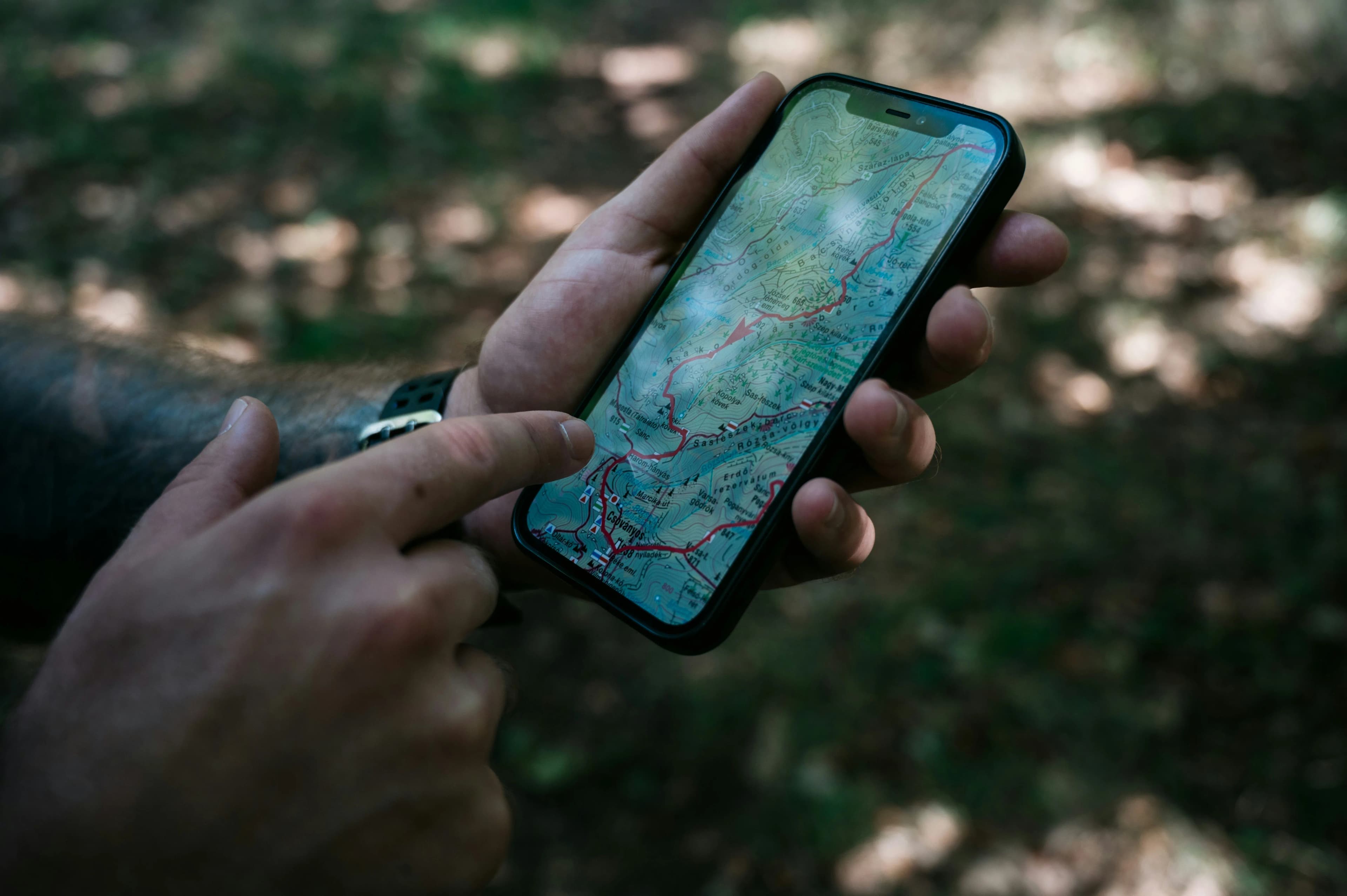 Hands holding a phone showing a GPS hiking map with a red route line in woodland