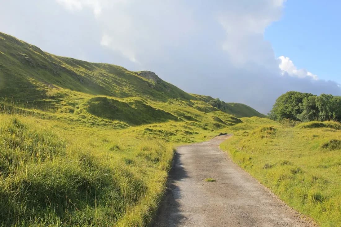 The Cotswold Way winding across open grassland and limestone hummocks on Cleeve Hill under a partly cloudy sky