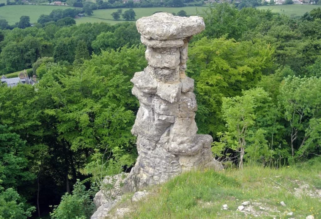 The Devil's Chimney, a tall limestone rock pillar on the edge of Leckhampton Hill above woodland